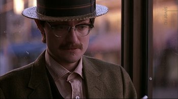 Movie still from “American Splendor” (2003), directed by Shari Springer Berman – A man wearing a hat and glasses standing in front of a window; Close Up shot, Over the shoulder angle
