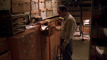 Movie still from “American Splendor” (2003), directed by Shari Springer Berman – A man standing in front of a row of filing cabinets; Medium shot, High angle