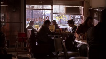 Movie still from “American Splendor” (2003), directed by Shari Springer Berman – A group of people sitting at a table in front of a window; Wide shot, Over the shoulder angle