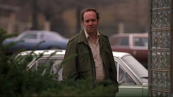 Movie still from “American Splendor” (2003), directed by Shari Springer Berman – A man standing in a parking lot next to parked cars; Medium shot, Over the shoulder angle