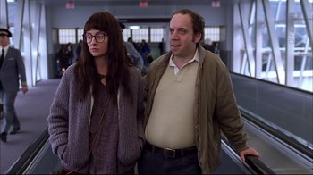 Movie still from “American Splendor” (2003), directed by Shari Springer Berman – A man and a woman standing next to each other in front of an escalator; Medium shot, Low angle