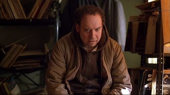 Movie still from “American Splendor” (2003), directed by Shari Springer Berman – A man in a brown jacket is sitting down; Medium shot, Low angle