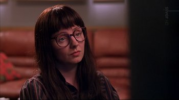 Movie still from “American Splendor” (2003), directed by Shari Springer Berman – A woman wearing glasses sitting in front of a couch; Close Up shot, Over the shoulder angle