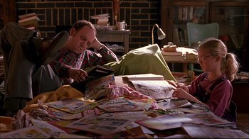 Movie still from “American Splendor” (2003), directed by Shari Springer Berman – A man reading a book while a woman looks at a pile of papers; Medium shot, High angle
