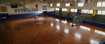 Movie still from “American Wedding” (2003), directed by Jesse Dylan – Two people standing in an empty gymnasium with bleachers; Extreme Wide shot, High angle