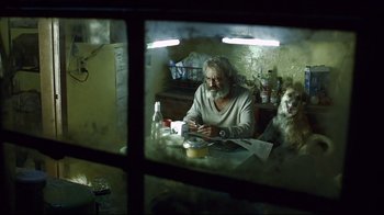 Movie still from “Amores Perros” (2000), directed by Alejandro G. Iñárritu – An older man sitting at a table with a dog looking through a window; Medium shot, Low angle