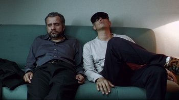 Movie still from “Amores Perros” (2000), directed by Alejandro G. Iñárritu – A couple of men sitting on top of a green couch; Medium shot, Low angle