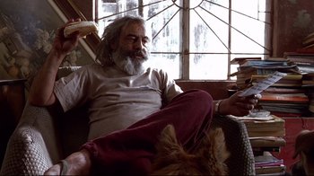Movie still from “Amores Perros” (2000), directed by Alejandro G. Iñárritu – An older man sitting on a couch eating a sandwich; Medium shot, Low angle