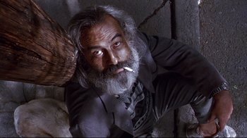 Movie still from “Amores Perros” (2000), directed by Alejandro G. Iñárritu – An old man with a long gray beard smoking a cigarette; Medium shot, Overhead angle