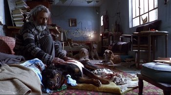 Movie still from “Amores Perros” (2000), directed by Alejandro G. Iñárritu – A man sitting on the floor with a dog and other dogs; Wide shot, High angle