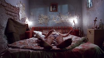 Movie still from “Amores Perros” (2000), directed by Alejandro G. Iñárritu – A man laying on a bed with his legs crossed; Wide shot, Low angle