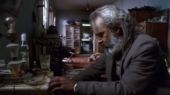 Movie still from “Amores Perros” (2000), directed by Alejandro G. Iñárritu – An older man sitting at a table in a cluttered room; Medium shot, Low angle