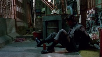 Movie still from “Amores Perros” (2000), directed by Alejandro G. Iñárritu – A man sitting on the ground next to a trash can; Wide shot, High angle