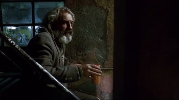 Movie still from “Amores Perros” (2000), directed by Alejandro G. Iñárritu – An older man sitting on a ledge holding a cup; Medium shot, Low angle
