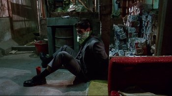 Movie still from “Amores Perros” (2000), directed by Alejandro G. Iñárritu – A man sitting on the ground wearing a mask; Wide shot, High angle