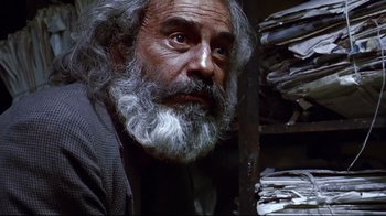 Movie still from “Amores Perros” (2000), directed by Alejandro G. Iñárritu – An old man with a beard is sitting in front of a stack of papers; Close Up shot, Low angle