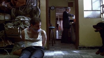 Movie still from “Amores Perros” (2000), directed by Alejandro G. Iñárritu – A man in a white tank top is sitting on the floor; Wide shot, Low angle