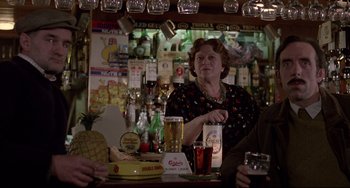 Movie still from “An American Werewolf in London” (1981), directed by John Landis – An older woman standing at a bar with a pineapple; Medium shot, Over the shoulder angle