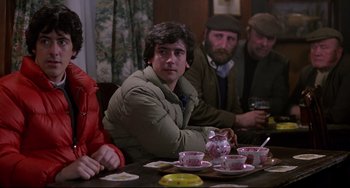 Movie still from “An American Werewolf in London” (1981), directed by John Landis – A group of people sitting at a table with cups and saucers on it; Medium shot, Over the shoulder angle