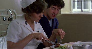 Movie still from “An American Werewolf in London” (1981), directed by John Landis – A woman in a nurse's uniform cutting vegetables with a knife and a fork; Close Up shot, Over the shoulder angle
