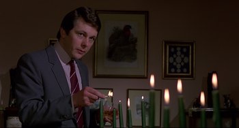 Movie still from “An American Werewolf in London” (1981), directed by John Landis – A man in a suit lighting candles in a living room; Medium shot, Low angle