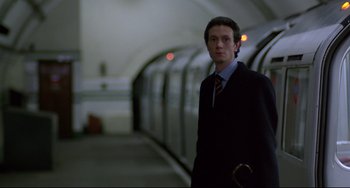 Movie still from “An American Werewolf in London” (1981), directed by John Landis – A man in a suit and tie standing in front of a train; Medium shot, Low angle