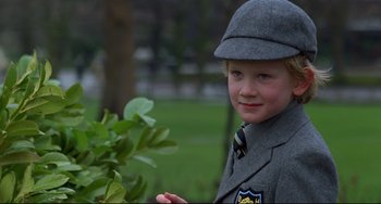 Movie still from “An American Werewolf in London” (1981), directed by John Landis – A young boy in a suit and hat is standing in front of a tree; Close Up shot, Over the shoulder angle