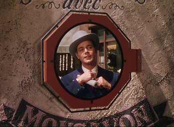 Movie still from “An American in Paris” (1951), directed by Vincente Minnelli – A man in a suit and a white hat is holding a cup; Medium shot, Low angle