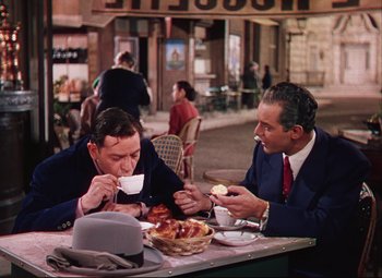 Movie still from “An American in Paris” (1951), directed by Vincente Minnelli – A couple of men sitting at a table eating food; Medium shot, High angle