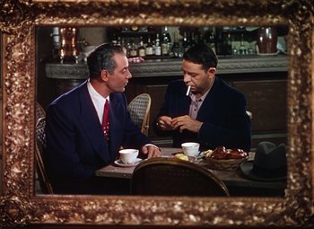 Movie still from “An American in Paris” (1951), directed by Vincente Minnelli – Two men sitting at a table talking to each other; Medium shot, High angle