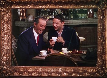 Movie still from “An American in Paris” (1951), directed by Vincente Minnelli – Two men sitting at a table looking at a cell phone; Medium shot, High angle