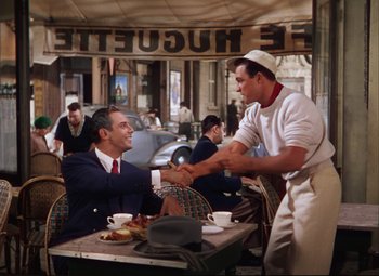 Movie still from “An American in Paris” (1951), directed by Vincente Minnelli – Two men shaking hands at an outdoor restaurant; Medium shot, Over the shoulder angle