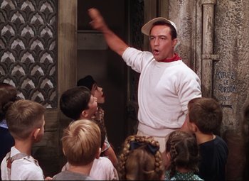 Movie still from “An American in Paris” (1951), directed by Vincente Minnelli – A group of children are gathered around a man in a white shirt; Medium shot, Low angle