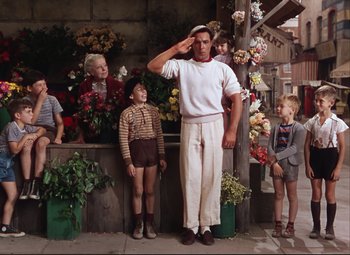 Movie still from “An American in Paris” (1951), directed by Vincente Minnelli – A man saluting in front of a group of children; Wide shot, Low angle