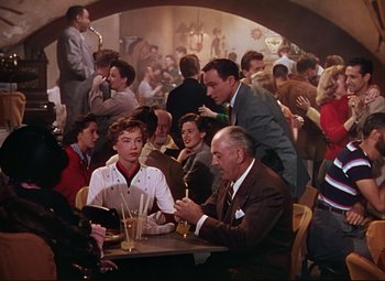 Movie still from “An American in Paris” (1951), directed by Vincente Minnelli – A group of people sitting at a table in a room; Wide shot, High angle