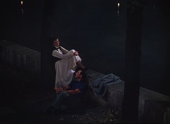 Movie still from “An American in Paris” (1951), directed by Vincente Minnelli – A man and a woman sitting on the ground; Wide shot, High angle