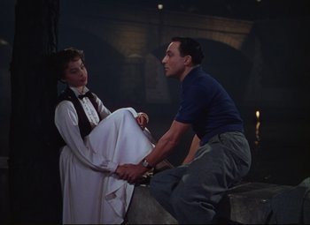 Movie still from “An American in Paris” (1951), directed by Vincente Minnelli – A man and a woman holding hands while sitting on top of a wall; Medium shot, High angle
