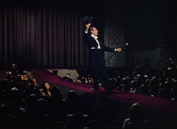 Movie still from “An American in Paris” (1951), directed by Vincente Minnelli – A man in a suit and top hat on a stage; Extreme Wide shot, Low angle