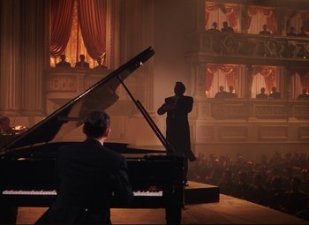 Movie still from “An American in Paris” (1951), directed by Vincente Minnelli – A man standing on a stage next to a grand piano; Wide shot, High angle