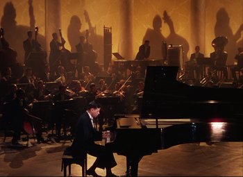 Movie still from “An American in Paris” (1951), directed by Vincente Minnelli – A man sitting at a grand piano in front of an orchestra; Extreme Wide shot, High angle