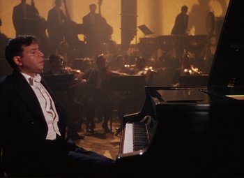 Movie still from “An American in Paris” (1951), directed by Vincente Minnelli – A man sitting at a grand piano in front of an orchestra; Medium shot, High angle