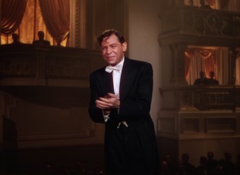 Movie still from “An American in Paris” (1951), directed by Vincente Minnelli – A man in a tuxedo claps his hands in front of an audience; Medium shot, Low angle