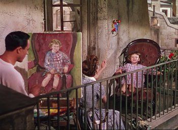 Movie still from “An American in Paris” (1951), directed by Vincente Minnelli – A woman sitting in a chair next to a painting of a boy; Wide shot, High angle