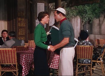 Movie still from “An American in Paris” (1951), directed by Vincente Minnelli – A man and a woman holding hands in front of a table; Medium shot, High angle