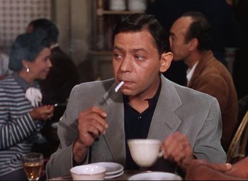 Movie still from “An American in Paris” (1951), directed by Vincente Minnelli – A man sitting at a table with a spoon in his mouth; Medium shot, High angle