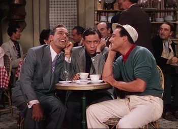 Movie still from “An American in Paris” (1951), directed by Vincente Minnelli – A group of men sitting at a table talking on cellphones; Medium shot, High angle