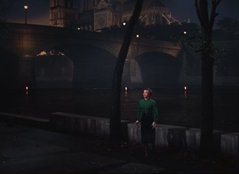 Movie still from “An American in Paris” (1951), directed by Vincente Minnelli – A woman in a green sweater standing next to a river; Wide shot, High angle