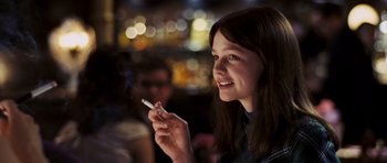 Movie still from “An Education” (2009), directed by Lone Scherfig – A woman holding a cigarette in her hand and smiling; Close Up shot, Over the shoulder angle