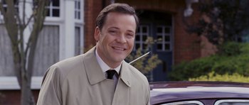 Movie still from “An Education” (2009), directed by Lone Scherfig – A man in a trench coat standing in front of a car; Close Up shot, Over the shoulder angle