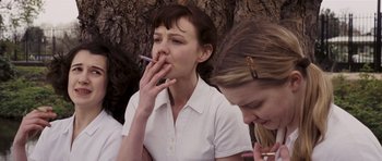 Movie still from “An Education” (2009), directed by Lone Scherfig – A woman smoking a cigarette while sitting next to another woman; Medium shot, Low angle